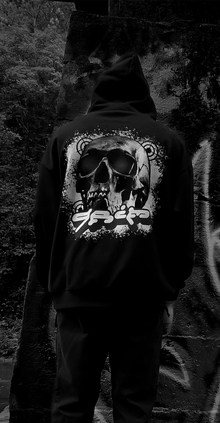 Black streetwear hoodie with large skull design by KIBISHI, styled in front of urban graffiti wall — artistic and edgy clothing for modern street culture.